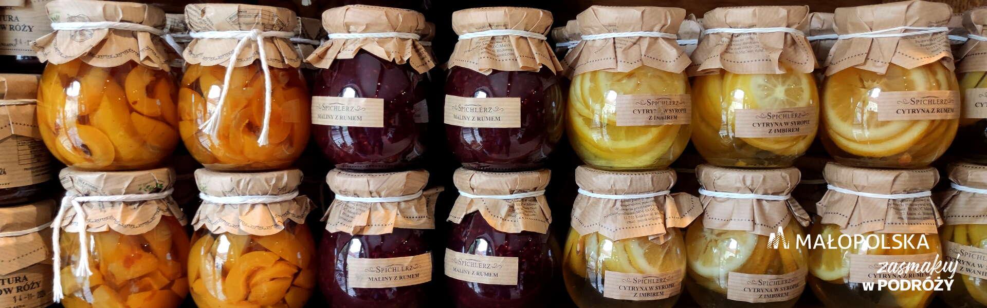 A shelf full of jars of peaches, raspberries and lemons in syrup, in the bottom right corner the logo of Malopolska (Lesser Poland) and the inscription ‘Enjoy your journey’