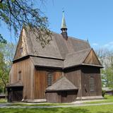 Drewniany kościół z sygnaturką na dachu, otoczony niskim drewnianym ogrodzeniem, obok kilka drzew, trawa.