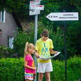 Dwoje dzieci: chłopiec trzymający rozłożoną mapę i dziewczynka przy drogowskazie do Jaskini Wierzchowskiej