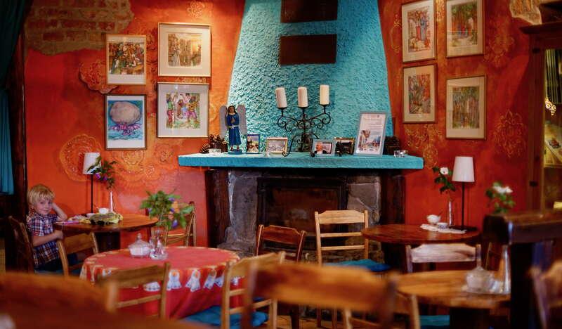 Wnętrze kawiarni Cafe Pencjonat w Lackoronie z pomalowanym na niebiesko kominkiem, czerwonymi ścianami, na których wiszą obrazy, przy jednym z okręgłych stolikó siedzi kilkuletni chłopiec