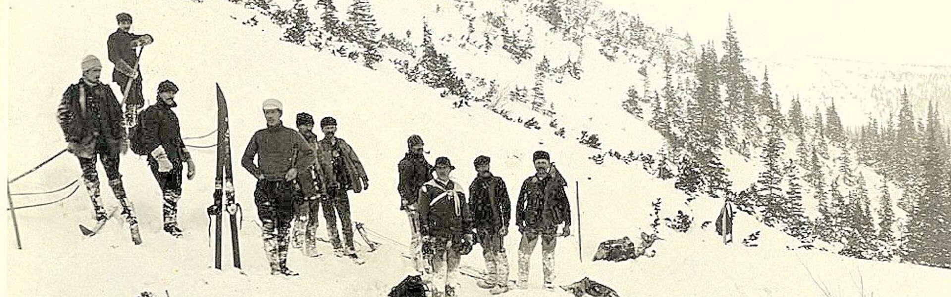 Grupa mężczyzn w strojach z początku wieku XX stojących na śniegu