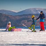 Narciarze i snowboardzistka ubrani w kolorowe stroje narciarskie na ośnieżonej łączce na tle gór