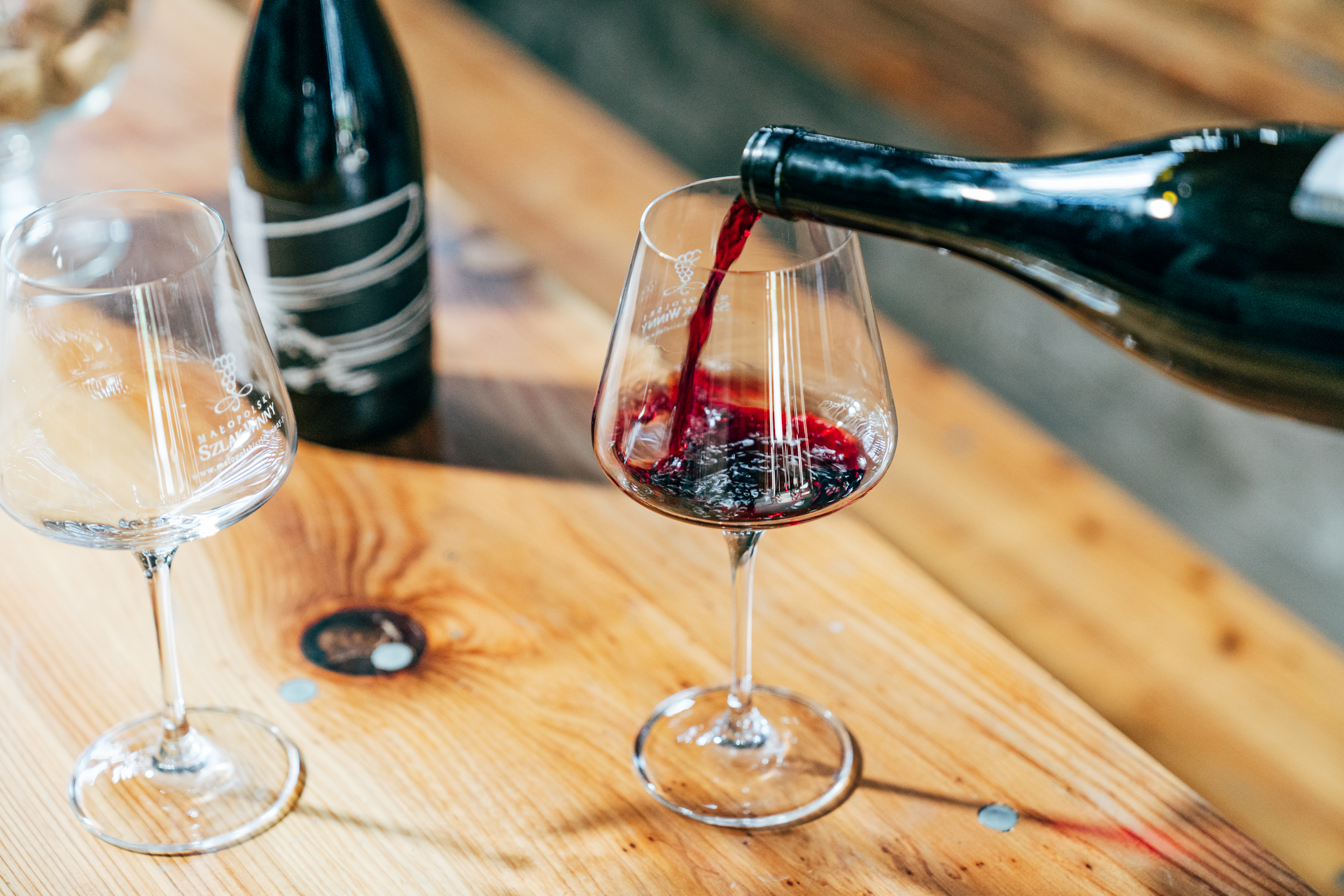 Czerwone wino leje się z butelki trafiając do szklanego kieliszka