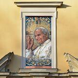 W oknie nad ozdobnym gzymsem, w całej jego ramie kolorowa mozaika autorstwa Magdaleny Czeskiej przedstawiająca popiersie papieża Jana Pawła II z uśmiechniętą buzią, z siwymi włosami, z uniesioną błogosławiącą prawą ręką, w białej albie z wiszącym krzyżem i z białą piuską na głowie. W tle rozjaśniony krzyż i wokoło kwiaty.