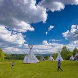 Namioty indiańskie tipi na łące w otoczeniu zieleni w porze wiosennej, pomiędzy namiotami bawiące się dzieci