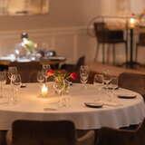 Zbliżenie na okrągły, nakryty stół w Restauracji Farina w Krakowie z kieliszkami i różami w wazonie na środku.